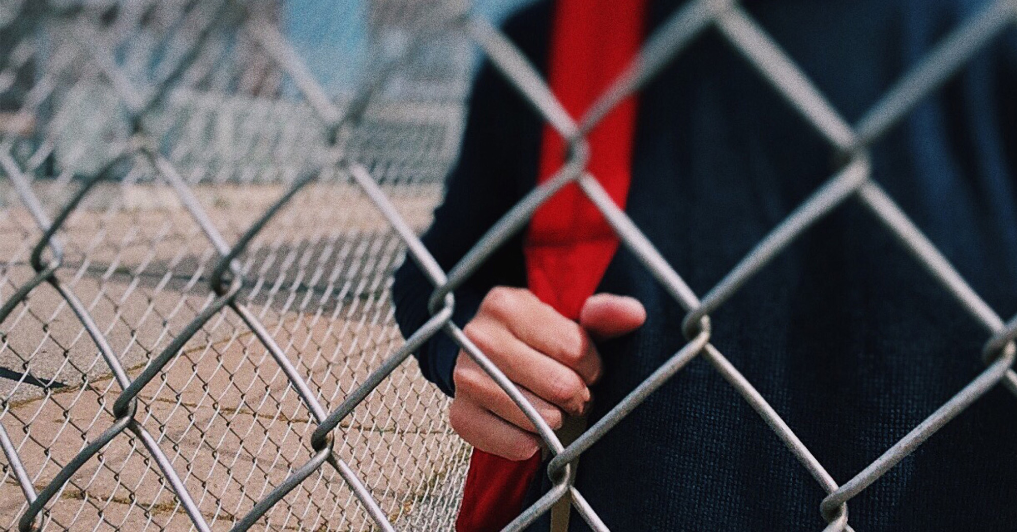 Hand holding red scarf in front of a fence
